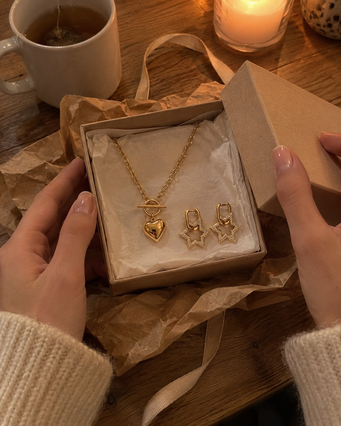 Hands holding a small open gift box with a gold necklace, kraft paper and ribbon on a table