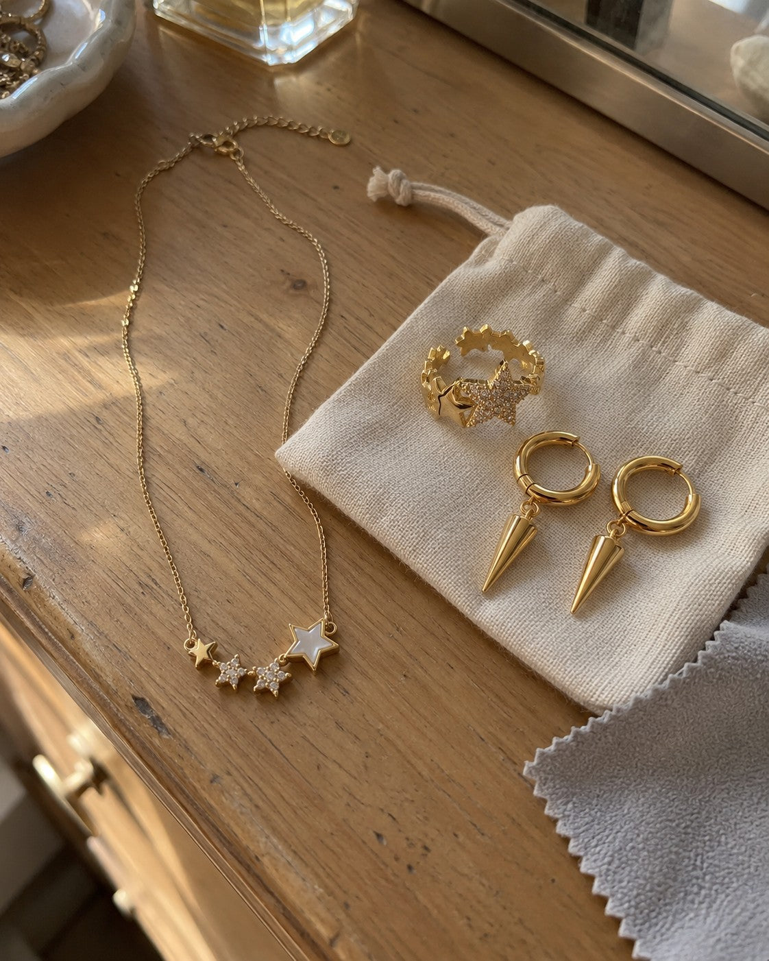 Gold jewelry laid on a beige cotton pouch next to a soft cloth on a wooden dresser