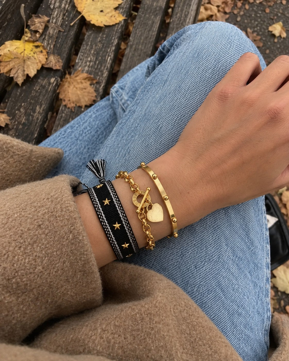 Wrist wearing a braided bracelet, a gold heart bracelet and a gold steel bracelet stacked together